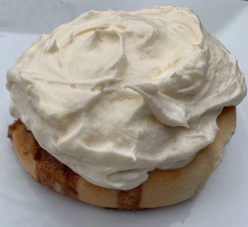 A freshly baked cinnamon roll topped with a generous swirl of creamy frosting.