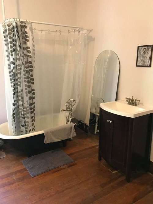 A bathroom featuring a clawfoot tub with a shower curtain, a sink cabinet, and a mirror against a light-colored wall.