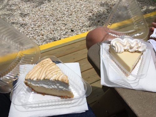 Two slices of pie in clear containers, one with a caramel topping and the other with whipped cream, on a table.