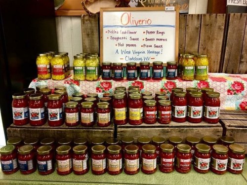 A display of various jars of sauces and pickled vegetables on wooden shelves, with a sign reading "Oliverio."
