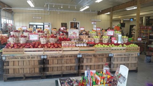 A vibrant market display with baskets of apples, snacks, and various produce in a rustic setting.