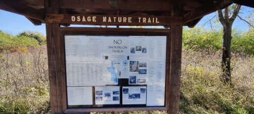 A wooden sign for Osage Nature Trail displaying rules and information, surrounded by tall grass and trees.