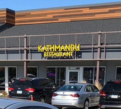 A restaurant building with a bright yellow sign reading "KATHMANDU" and several parked cars in front.