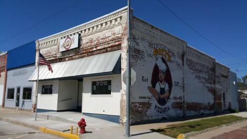 A brick building with a mural of a chef holding a pizza, featuring an awning and an American flag outside.