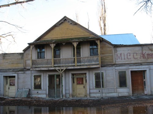 Abandoned two-story building with a wooden facade, balcony, and peeling paint, reflecting a sense of decay.