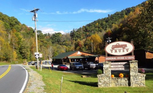 A scenic view of a general store and café named "Trust," surrounded by autumn foliage and mountains.