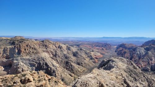 A panoramic view of rugged mountains and valleys under a clear blue sky, showcasing vibrant rock formations.