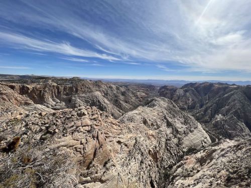 A panoramic view of rugged mountains and valleys under a blue sky with wispy clouds.