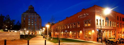 A scenic view of a brick tavern and a tall building at night, illuminated by streetlights in a quiet urban setting.