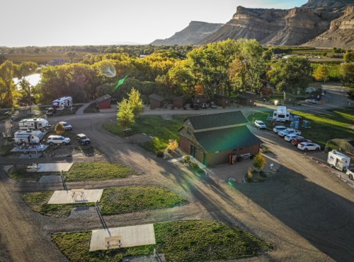 Aerial view of a campground with RVs, cabins, and trees, set against a backdrop of hills and a river.