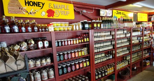 A colorful display of jars and bottles filled with honey, maple syrup, and jams on wooden shelves in a shop.