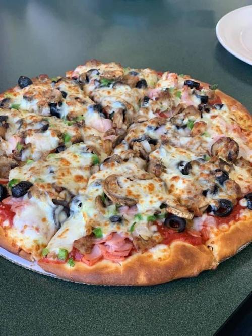 A freshly baked pizza topped with cheese, olives, mushrooms, ham, and green peppers on a golden crust.