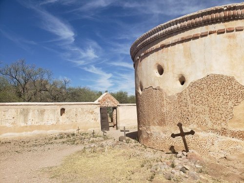 A historic stone structure with a round wall, surrounded by a dirt path and sparse vegetation under a blue sky.