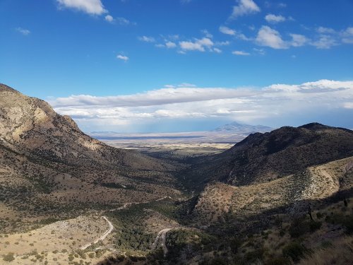 A panoramic view of a valley surrounded by mountains under a partly cloudy sky.