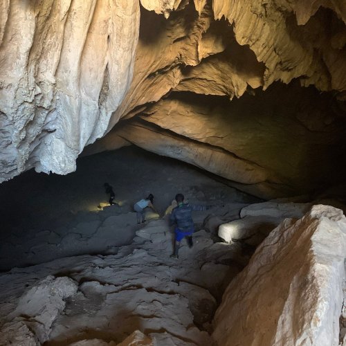 A dimly lit cave with rocky formations and people exploring the uneven terrain.