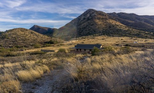 A house nestled in a dry, grassy landscape with mountains in the background under a clear sky.