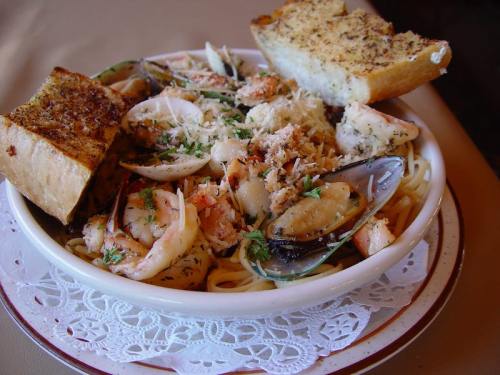 A bowl of seafood pasta topped with herbs and garlic bread on the side.