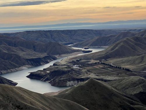 A scenic view of rolling hills and a winding river at sunset, with fields visible along the riverbanks.