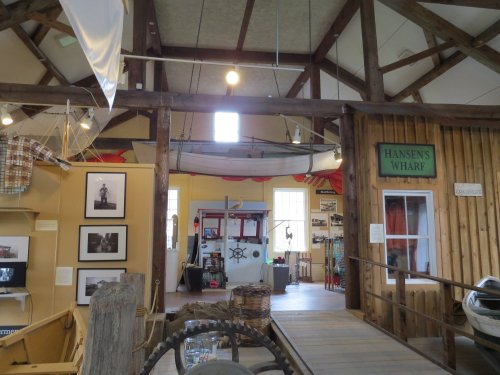 Interior of a maritime museum featuring boats, photographs, and wooden beams, with a sign reading "Hansen's Wharf."