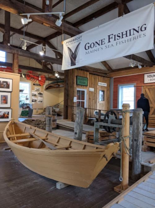 A wooden boat on display in a fishing museum, with informational banners and historical photos in the background.
