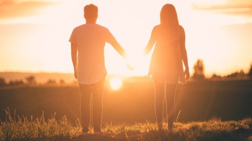 A couple holding hands at sunset, silhouetted against a warm, glowing sky.