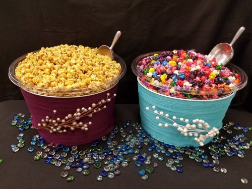Two large bowls filled with popcorn and colorful candy, surrounded by decorative glass gems on a black background.