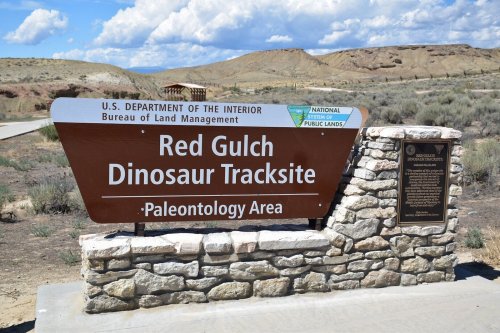 Sign for Red Gulch Dinosaur Tracksite, a paleontology area managed by the Bureau of Land Management. Scenic landscape in background.