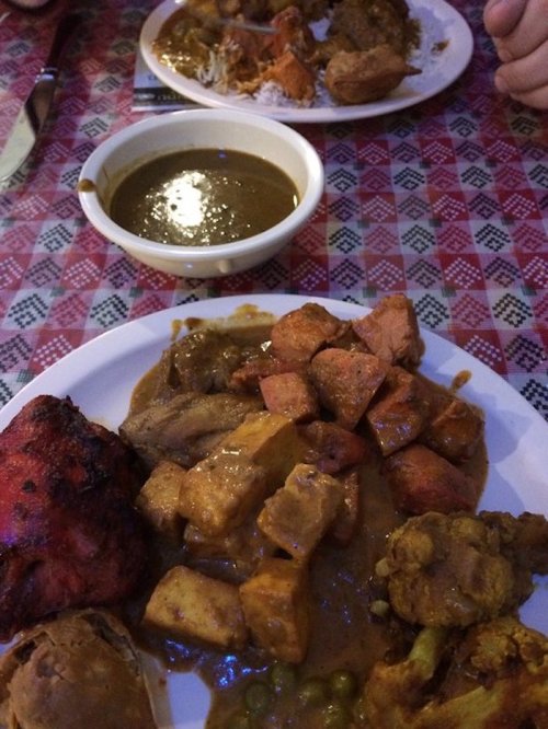 Two plates of Indian food featuring curry, rice, chicken, and assorted vegetables on a patterned tablecloth.