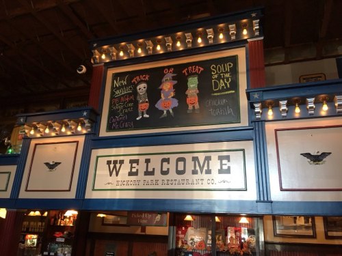 A restaurant interior featuring a welcome sign and a chalkboard with Halloween-themed decorations and soup of the day.
