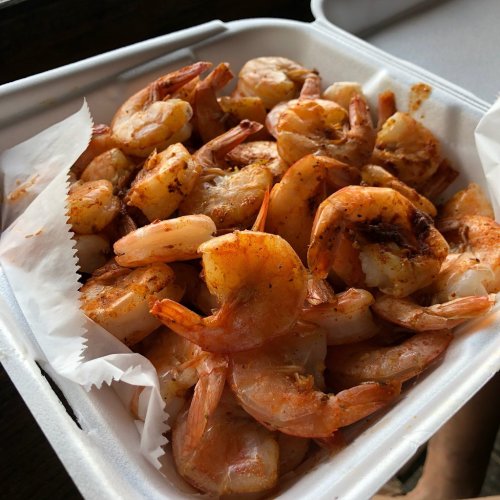 A container filled with seasoned, cooked shrimp, some with tails on, resting on a white paper liner.