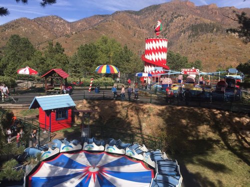 A colorful amusement park with rides, tents, and a scenic mountain backdrop on a sunny day.
