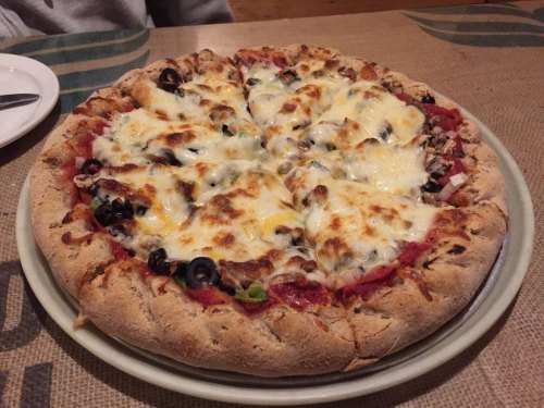 A freshly baked pizza with melted cheese, olives, and a thick crust, served on a round plate.