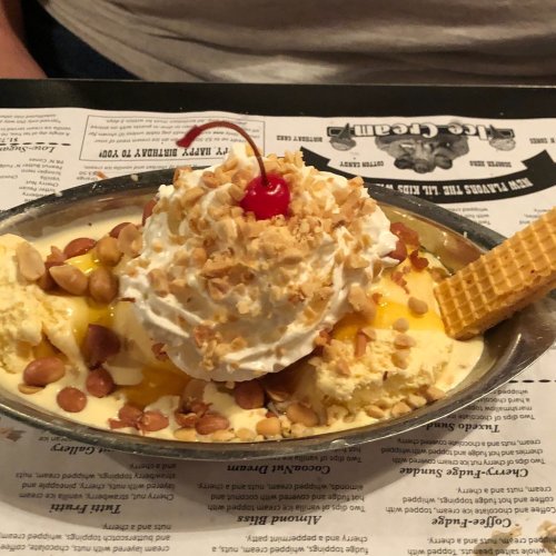 A delicious ice cream sundae topped with whipped cream, a cherry, crushed nuts, and a waffle cone on the side.