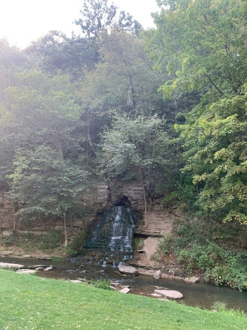 A serene waterfall cascading down rocky terrain, surrounded by lush green trees and a peaceful stream below.