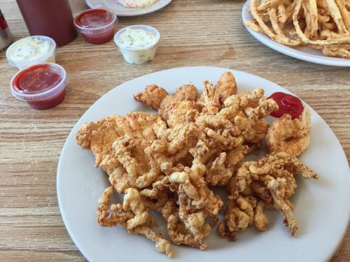 A plate of crispy fried seafood, including calamari and shrimp, served with dipping sauces on a wooden table.