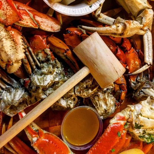 A variety of crabs and seafood arranged on a platter, with a wooden mallet and a small bowl of sauce.