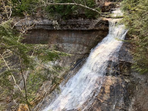 A serene waterfall cascading down rocky terrain, surrounded by lush greenery and trees.