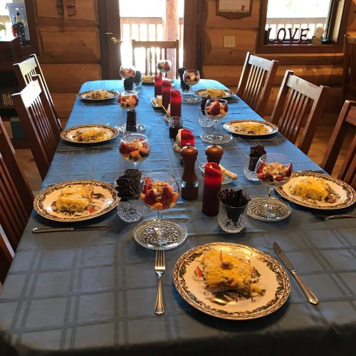 A beautifully set dining table with multiple plates of food, desserts, and drinks, surrounded by wooden chairs.