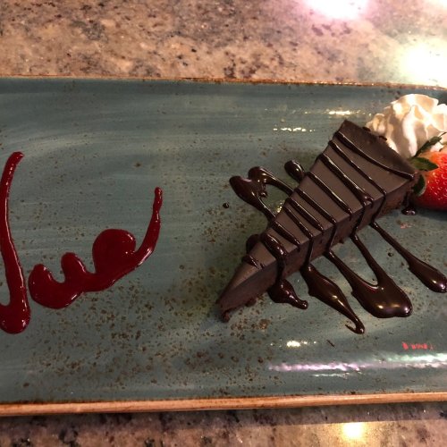 A slice of chocolate cake on a blue plate, garnished with whipped cream, a strawberry, and chocolate sauce.