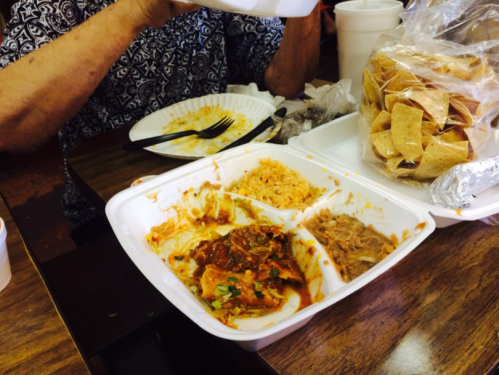 A partially eaten meal in a divided container with rice, beans, and sauce, alongside a bag of chips on a table.