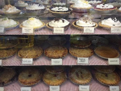 A display case filled with various pies, including chocolate, lemon, and fruit varieties, all topped with whipped cream.