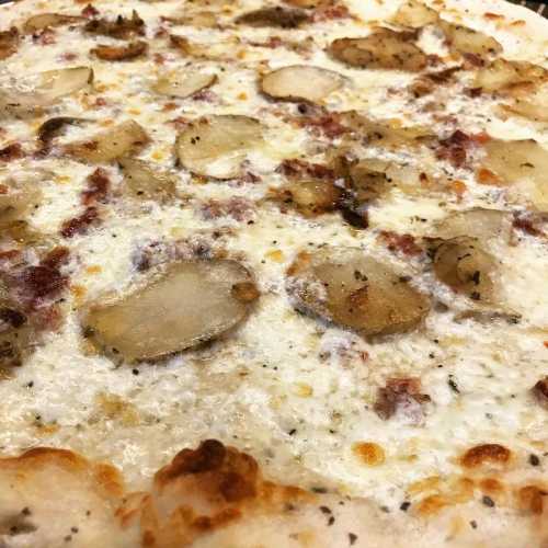 Close-up of a pizza topped with creamy white sauce, sliced potatoes, and herbs on a golden crust.