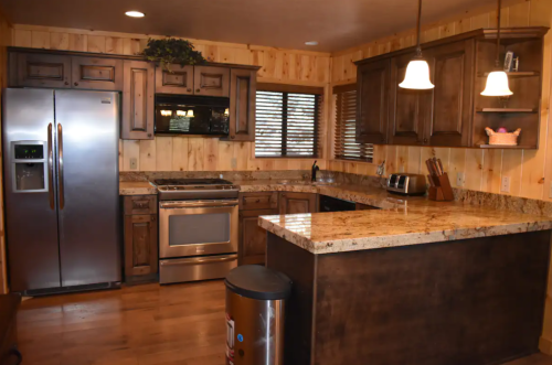 A cozy kitchen with wooden cabinets, granite countertops, stainless steel appliances, and warm lighting.