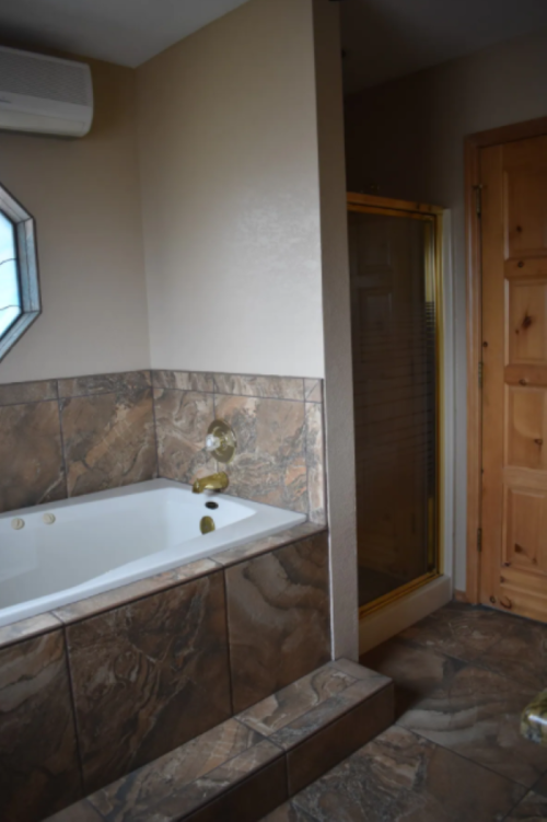 A bathroom featuring a jacuzzi tub, tiled walls, and a glass shower enclosure next to a wooden door.