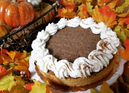 A pumpkin pie topped with whipped cream, surrounded by autumn leaves and decorative pumpkins.