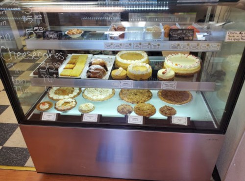 Display case filled with various desserts, including cheesecakes, cookies, and pastries, with prices labeled.