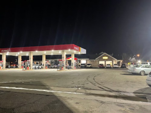 A gas station at night with several cars parked and a building in the background, illuminated by lights.