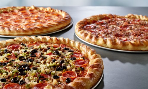 Three pizzas on a table: one with pepperoni, one with vegetables and pepperoni, and one with meat toppings.