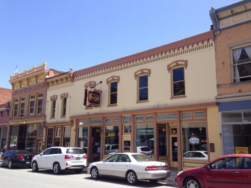 Historic buildings line a street, featuring colorful facades and parked cars under a clear blue sky.