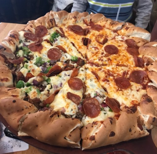 A large pizza with a stuffed crust, featuring pepperoni and a mix of toppings on one half, and cheese on the other.